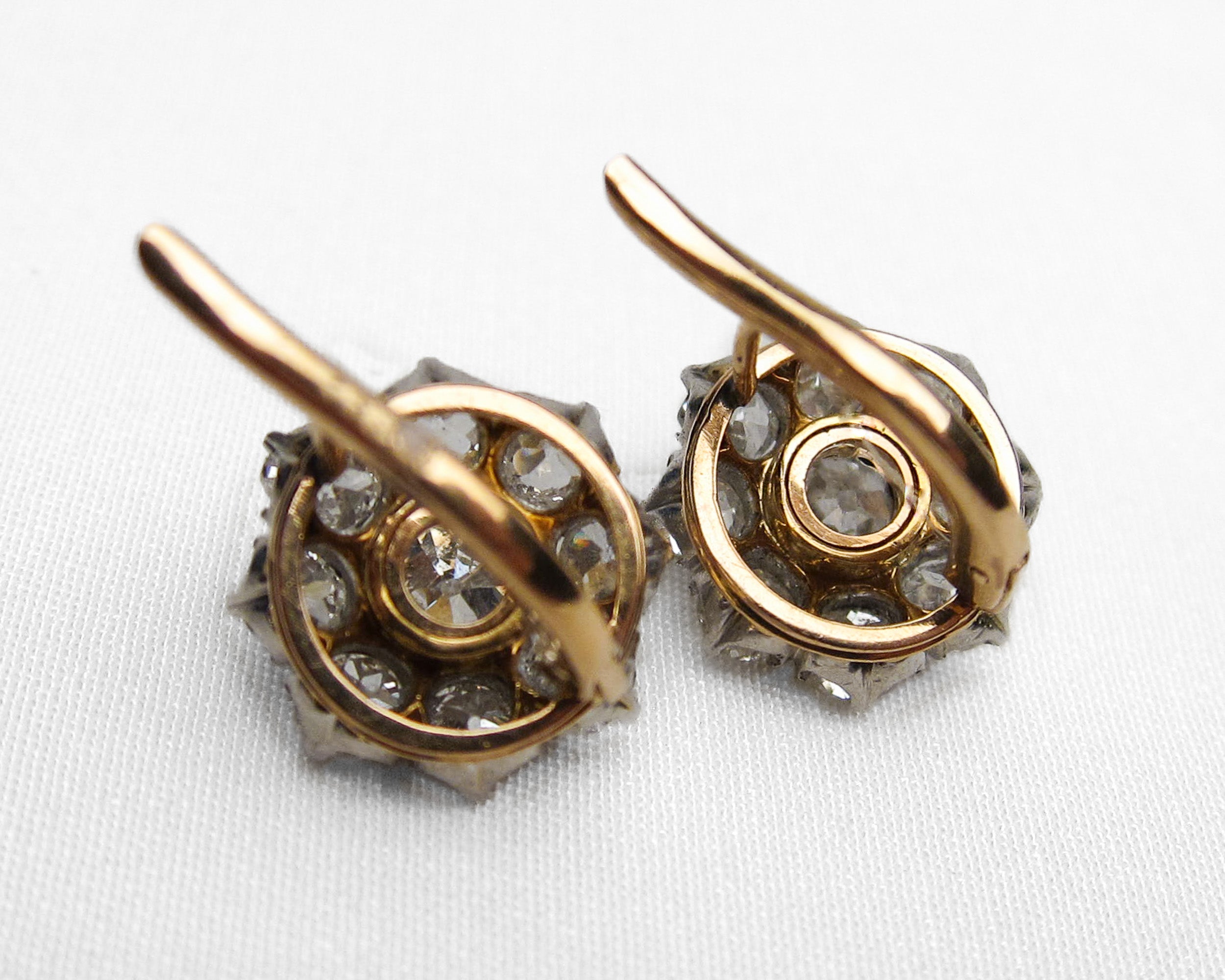 A pair of vintage gold and silver-toned earrings with clear gemstones, photographed on a white textured fabric background.