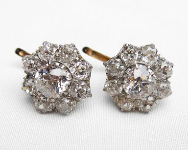 A pair of vintage-style diamond cluster stud earrings with a silver-toned setting and gold-toned post backs, displayed on a white textured fabric background.