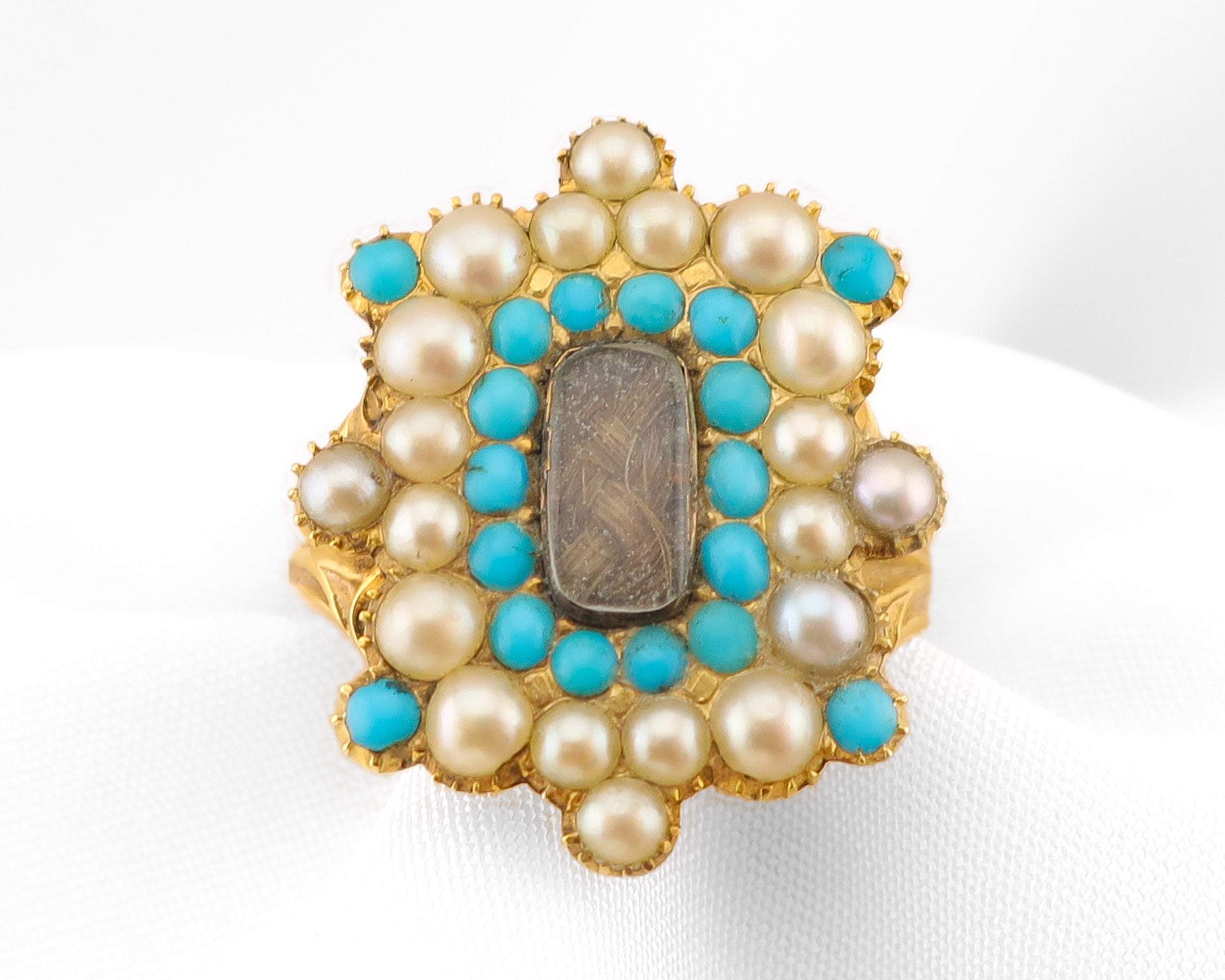 A vintage gold ring featuring a central rectangular brown stone surrounded by a double row of turquoise and white pearls in a floral cluster setting.