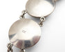 Close-up of a silver link bracelet showing a polished round disc link with a stamped 'FROM 925' hallmark on its flat surface, connected by small silver chains against a white background.