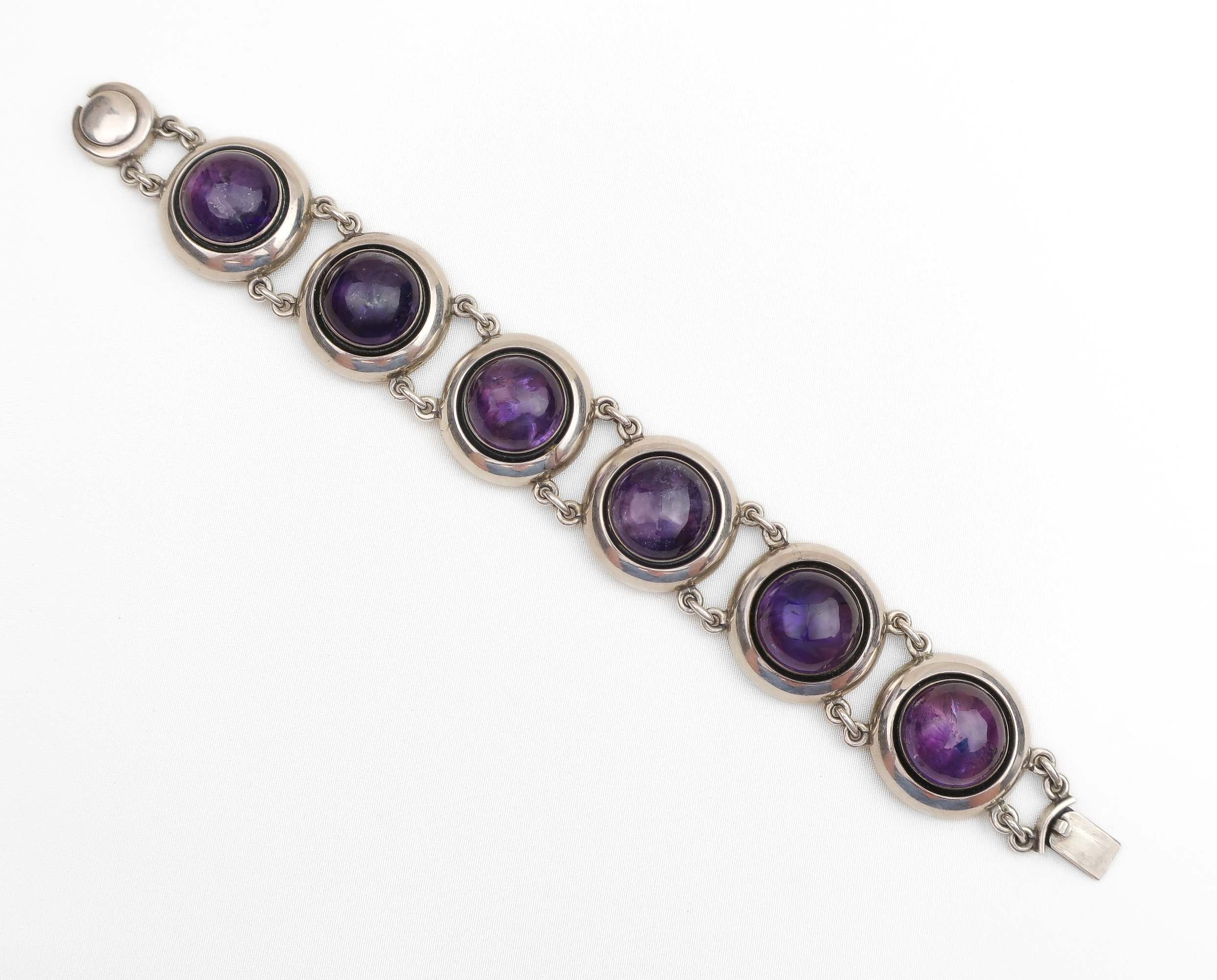 A silver-toned bracelet featuring five round bezel-set purple amethyst gemstones, displayed diagonally on a clean white background.