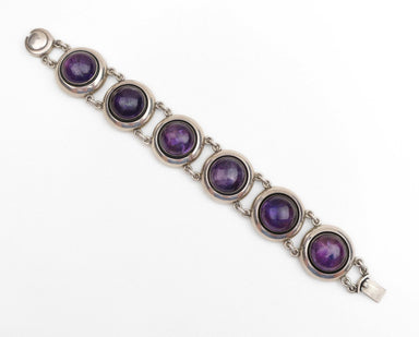 A silver-toned bracelet featuring five round bezel-set purple amethyst gemstones, displayed diagonally on a clean white background.