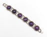 A silver-toned bracelet featuring five round bezel-set purple amethyst gemstones, displayed diagonally on a clean white background.