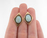 A pair of vintage-style gold diamond-shaped stud earrings with oval iridescent opal centers, shown resting on a person's fingers against a white background.